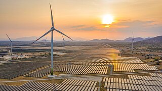 Ein Solarpark in dem Windkraftanlagen stehen. Die Sonne geht unter.