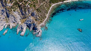 Aerial view of a section of coastline. Rocks and a road border the blue sea. 