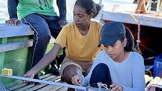 Two women sit in a boat and repair it. 