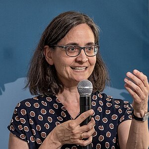 Birgit Schwenk stands between two bar tables and holds a microphone in her hand