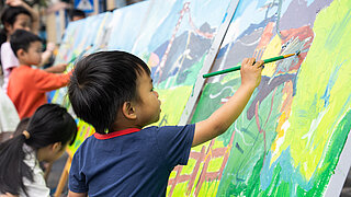 Ein Kind malt an einem großen Gemälde. 