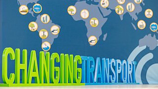 The lettering "Changing Transport" is displayed as a scuplture in front of a world map.